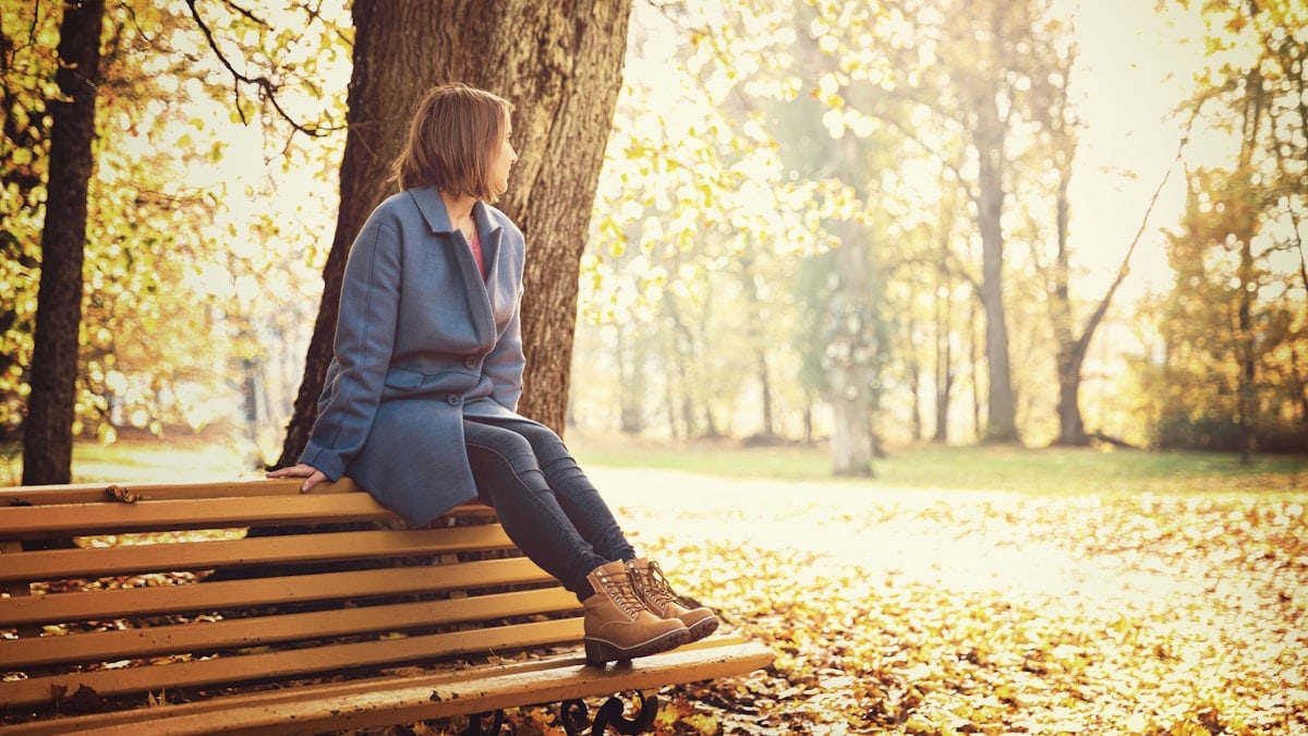 woman in blue blazer sitting on brown wooden bench during daytime