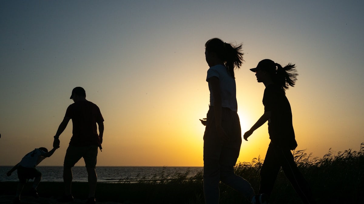 a group of people walking along a beach at sunset
